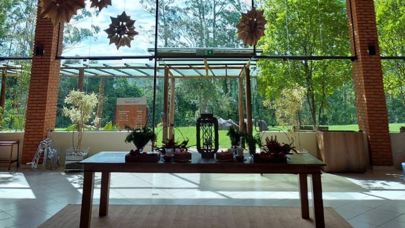 Salão envidraçado do Hotel Terras Altas com mesa decorada e vista para área verde externa.