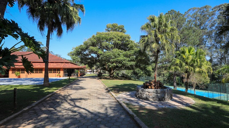 Caminho arborizado no Hotel Terras Altas com vista para quadra de tênis, paisagismo sustentável e área de convivência.