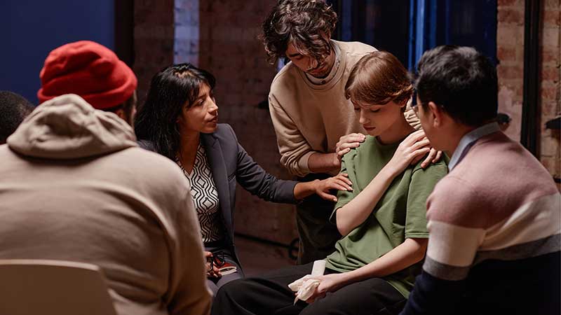 Grupo de apoio emocional, com pessoas oferecendo consolo e suporte a uma mulher visivelmente abalada