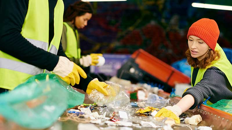 Grupo de voluntários com coletes verdes separando materiais recicláveis em estação de triagem de resíduos