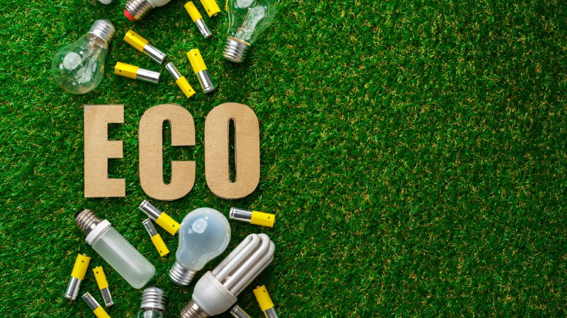 Blog Ambiental • Lâmpadas reutilizadas e a palavra "ECO" sobre grama artificial, representando soluções sustentáveis e economia circular.