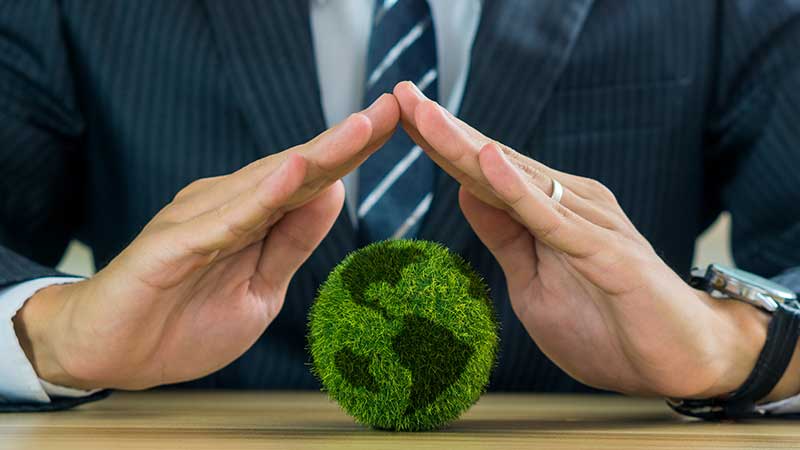 Blog Ambiental • Empresário protegendo um globo verde com símbolo ecológico, representando responsabilidade ambiental corporativa.