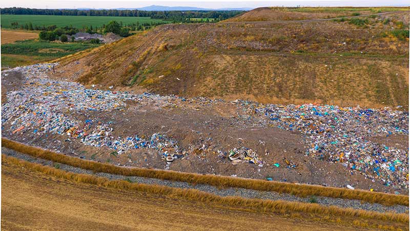 Vista aérea de aterro sanitário com grande acúmulo de resíduos sólidos ao lado de áreas agrícolas e vegetação.