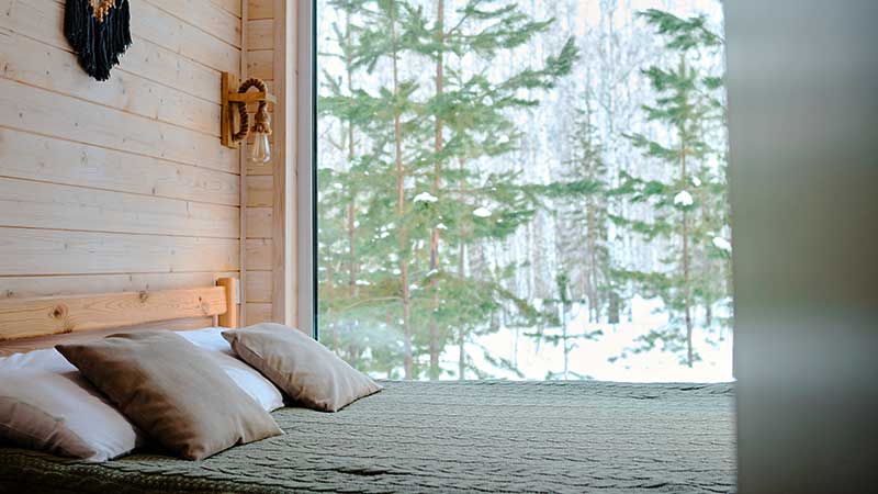 Quarto com decoração natural e vista para floresta nevada, simbolizando hospedagem ecológica integrada ao meio ambiente.