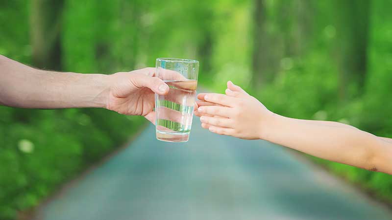 Blog Ambiental • Mão adulta entregando um copo de água a uma criança, simbolizando o acesso à água potável e a importância da preservação dos recursos hídricos.