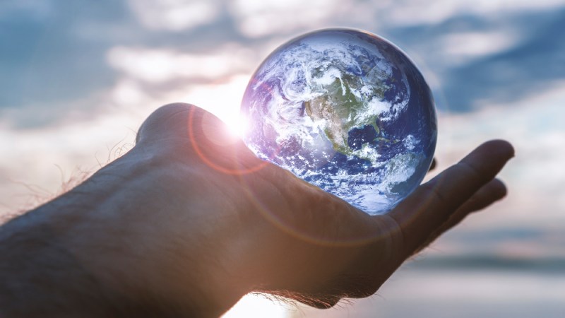 Blog Ambiental • Mão aberta segurando o planeta Terra com o pôr do sol ao fundo, simbolizando responsabilidade global e esperança por um futuro sustentável.